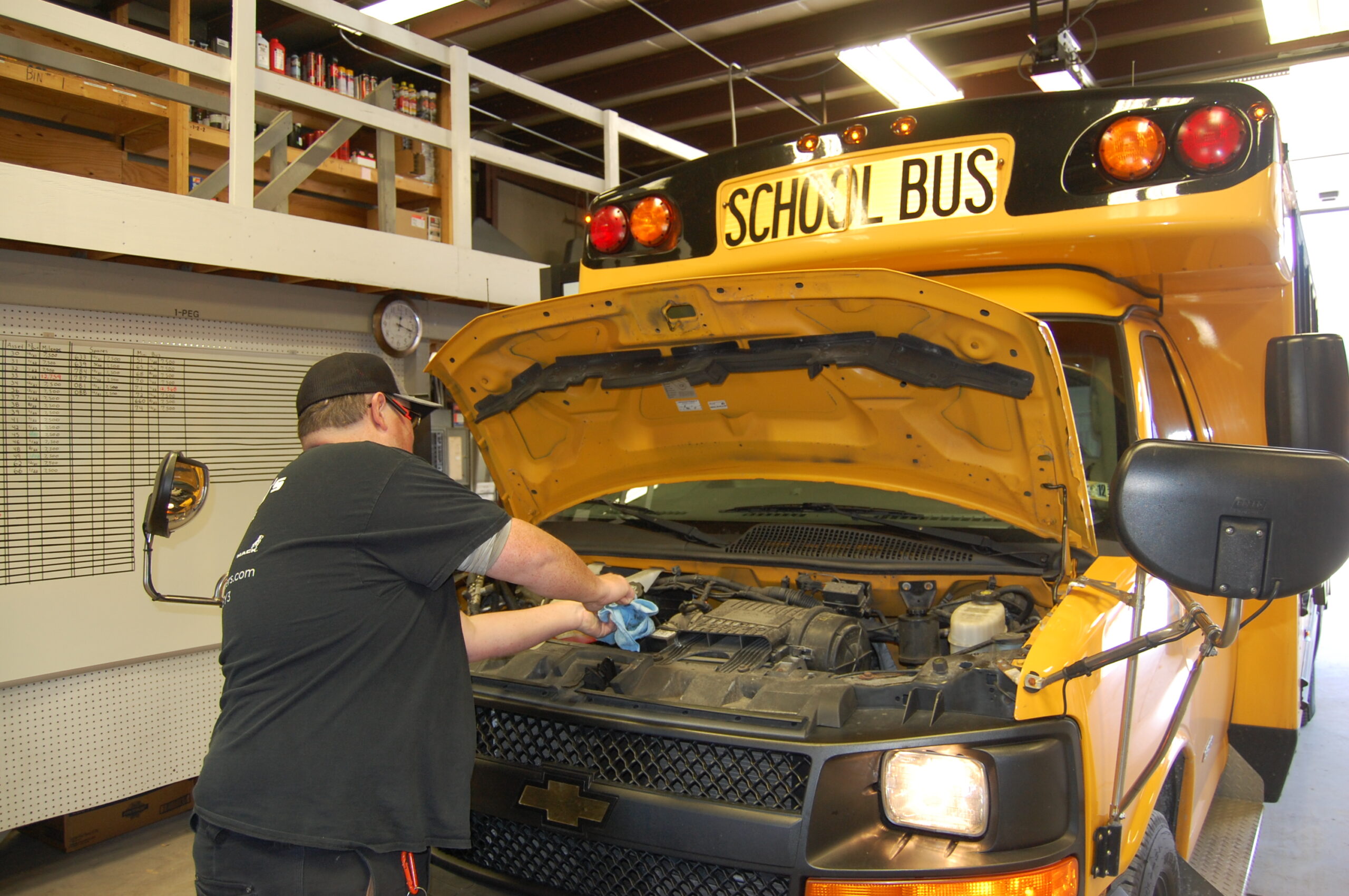 A mechanic checks the oil under the hood of a yellow bus.