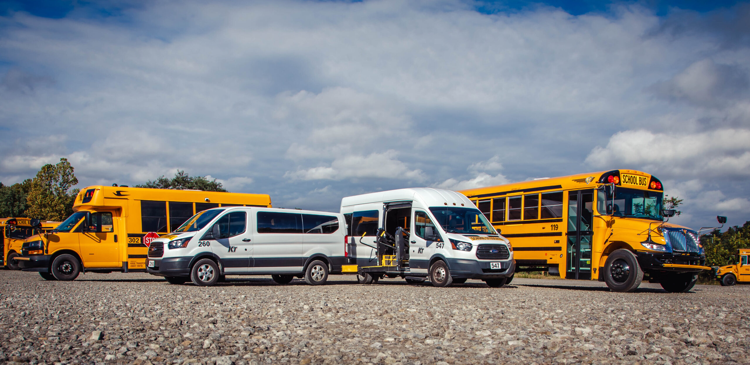 A fleet of yellow buses and white vans in a parking lot