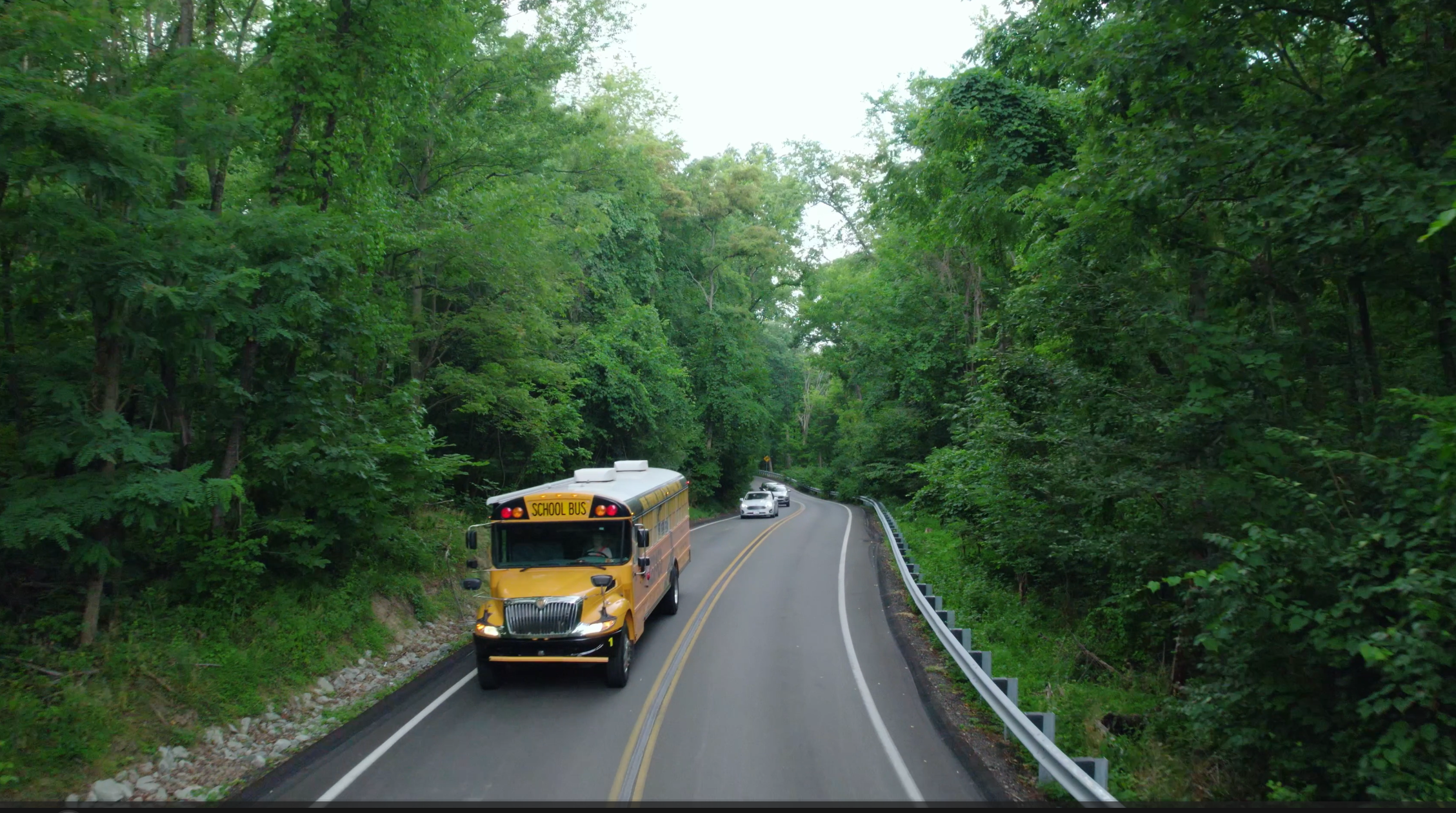 A yellow school bus travels on a winding road